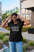 Woman wearing black Raised on Soca t-shirt outdoors with headphones